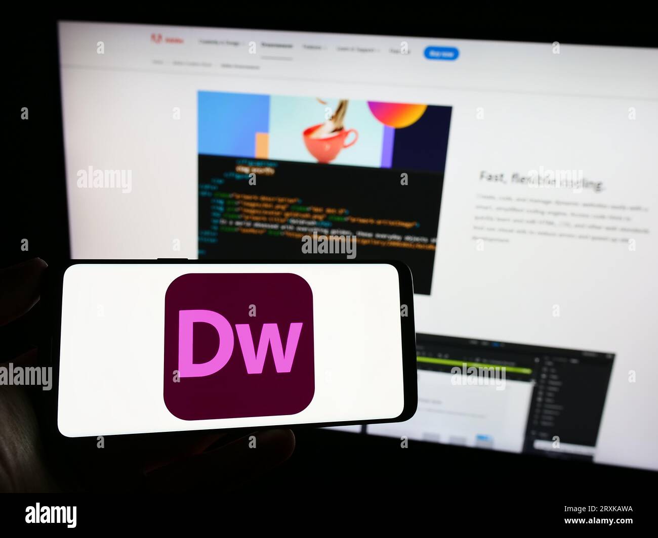 Person holding mobile phone with logo of web development software Adobe Dreamweaver on screen in front of web page. Focus on phone display. Stock Photo