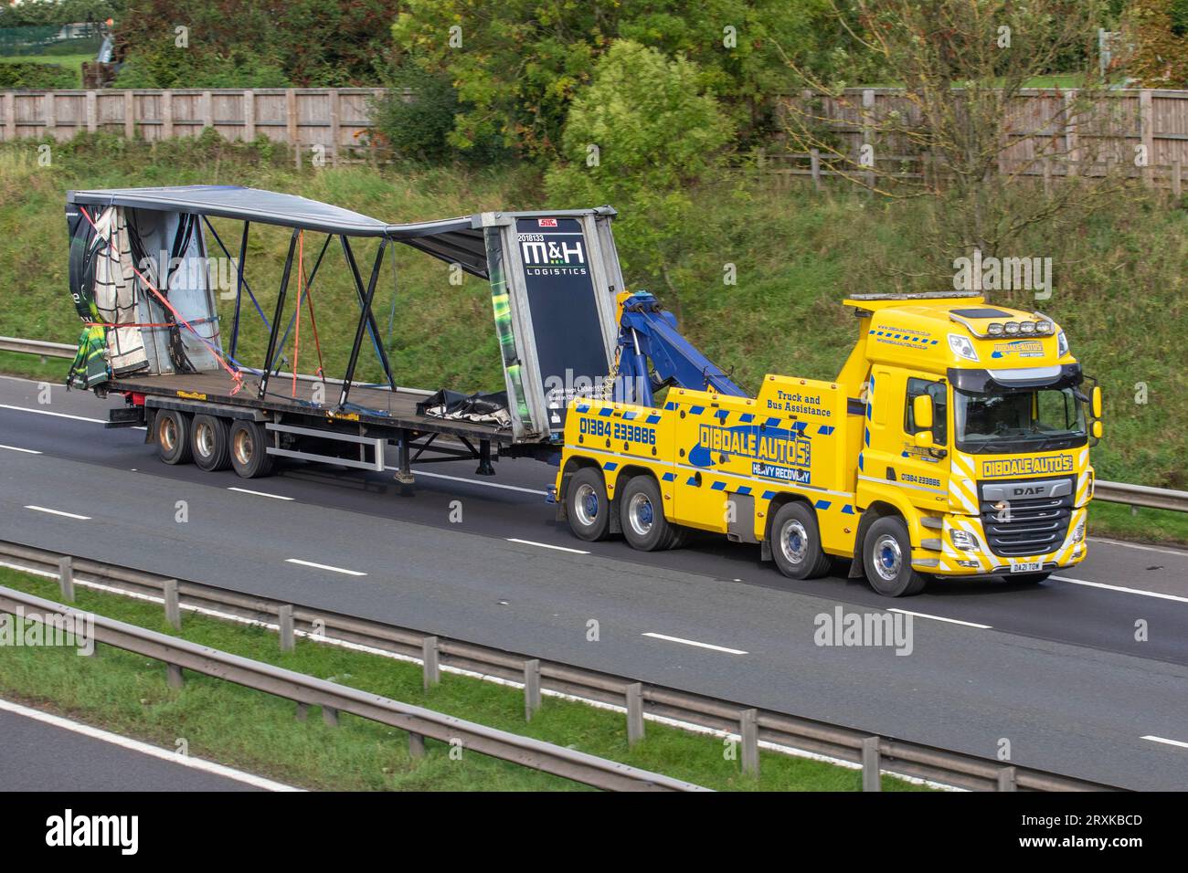 Collapsed, Accident damaged, deformed curtain-sided trailer being recovered by DibDale Autos heavy truck roadside rescue service; travelling at speed on the M6 motorway in Greater Manchester, UK Stock Photo
