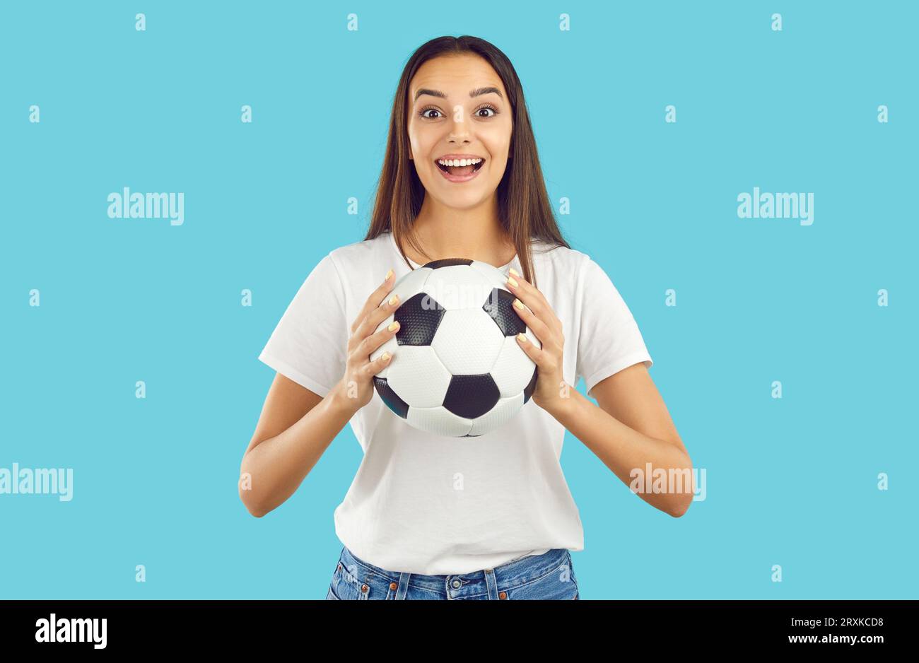 Soccer fan happy brunette girl holding football ball in hand on light blue background. Stock Photo