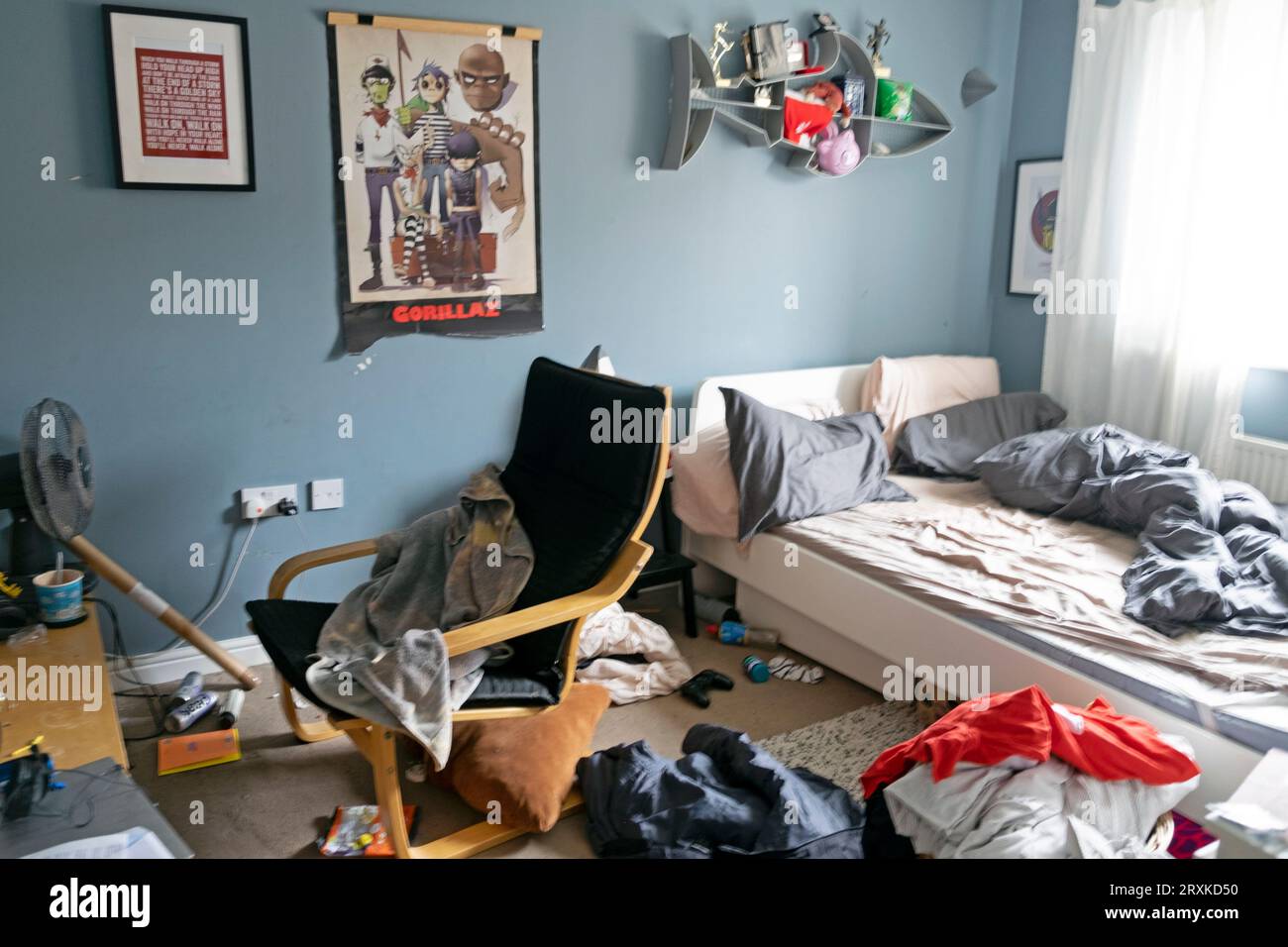 Messy bedroom of teenage teen boy and unmade bed clothes Gorillaz poster chair grey blue walls wall paint painted Great Britain UK 2023   KATHY DEWITT Stock Photo