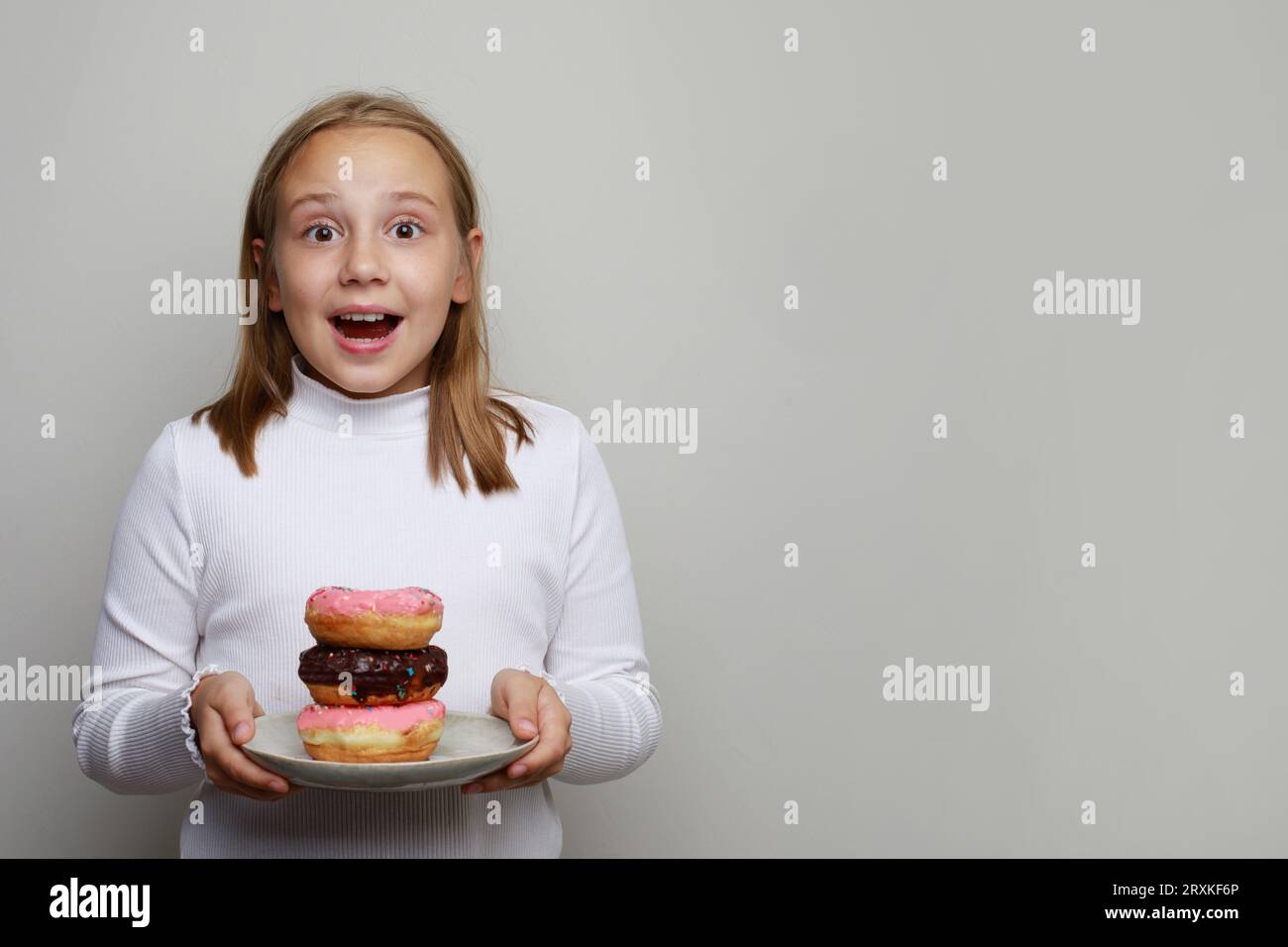 Cheerful happy surprised kid girl holding plate with colorful donut. Cute child having fun with doughnut  on white background. Sweet food, diet, happy Stock Photo