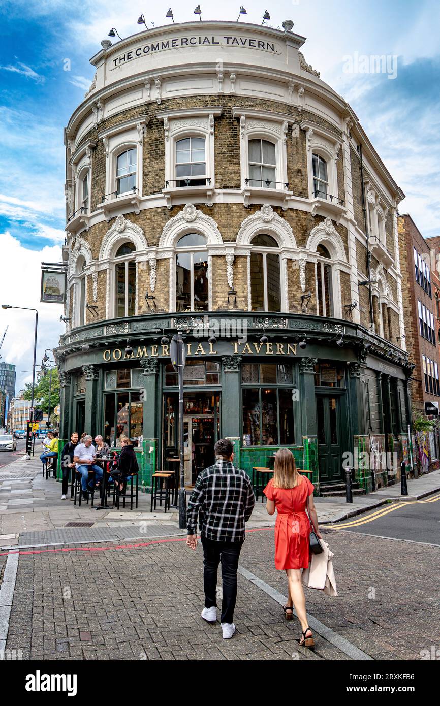 A man and a woman wearing a red dress entering The Commercial Tavern pub on Commercial Road, Spitalfields, London E1 Stock Photo