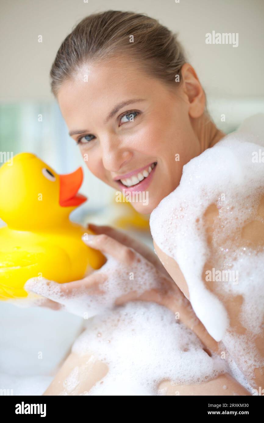 Woman smiling with a rubber duck in a bubble bath Stock Photo