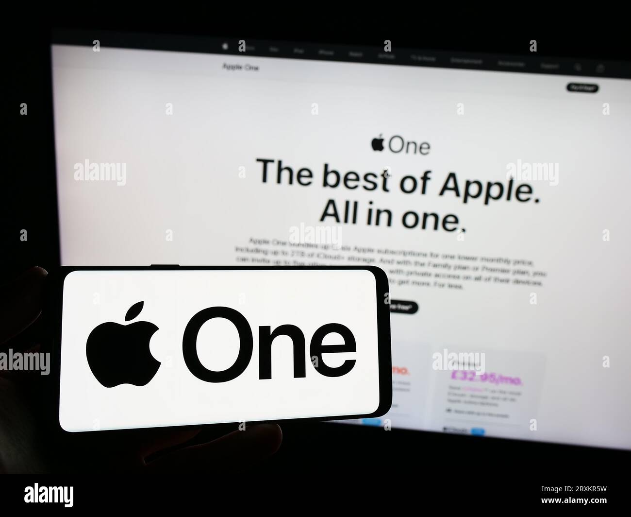 Person holding smartphone with logo of subscription service Apple One on screen in front of website. Focus on phone display. Stock Photo