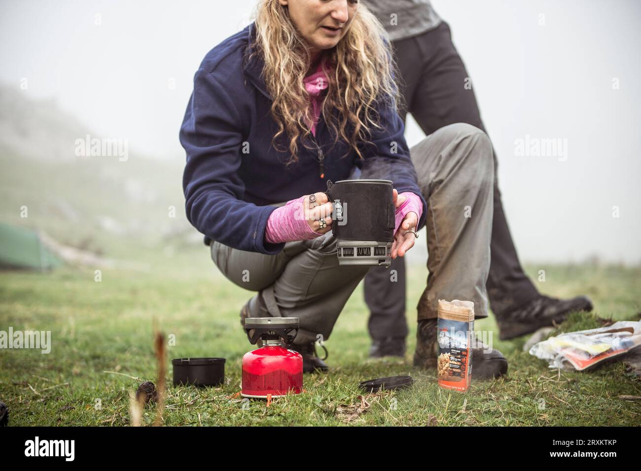 Young woman cooking at camp with portable stove Stock Photo