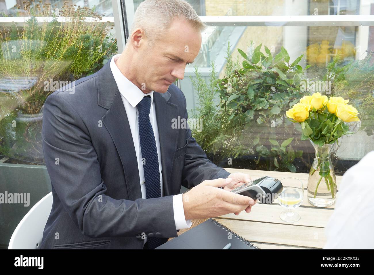 Businessman using EFTPOS machine at restaurant table Stock Photo