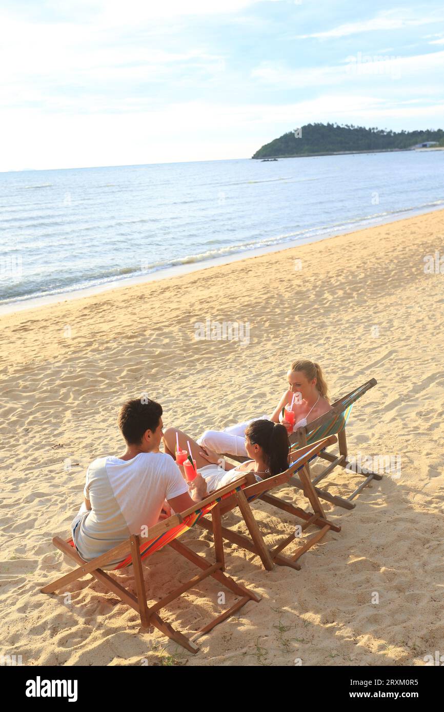Young people sitting on deck chairs on beach Stock Photo