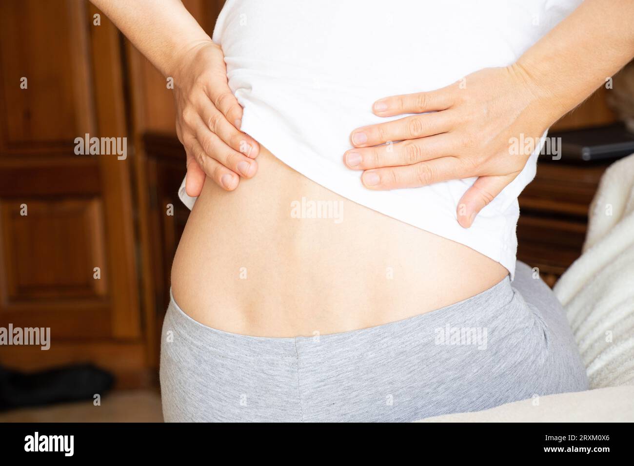 A young girl holds her back because of back pain, sitting on her bed at