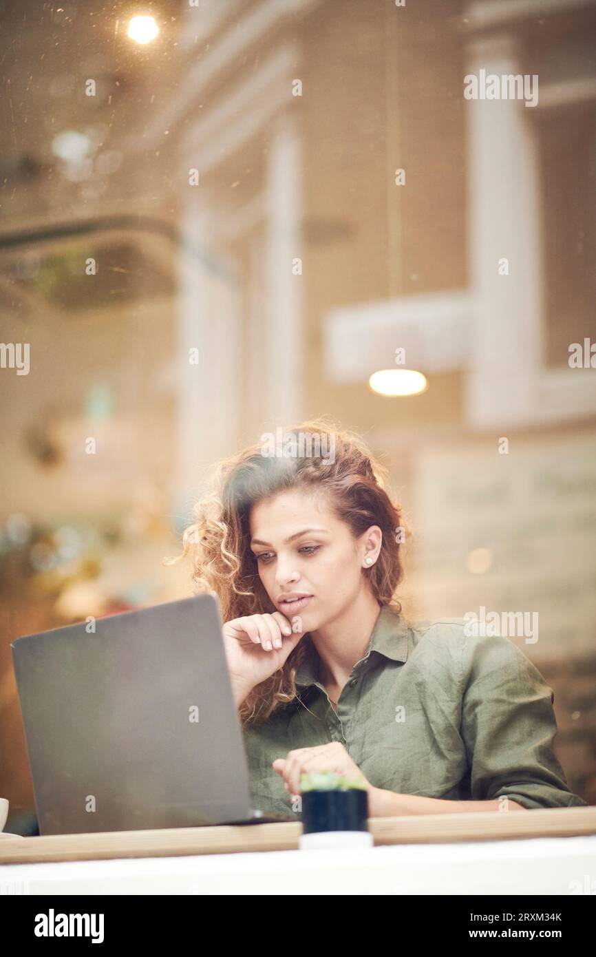 Young woman using laptop behind cafe window Stock Photo