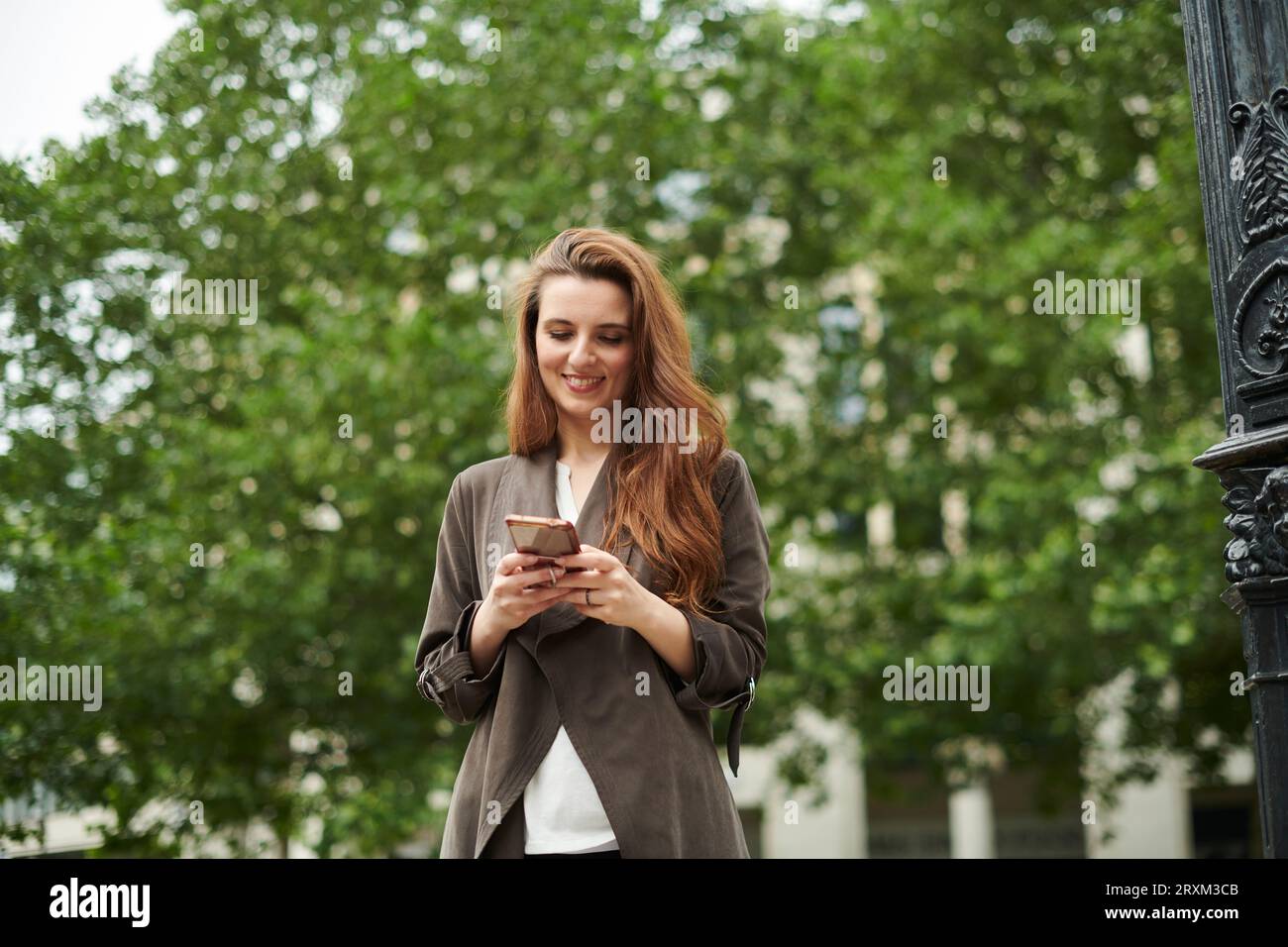 Mid adult woman smiling while texting on smart phone Stock Photo