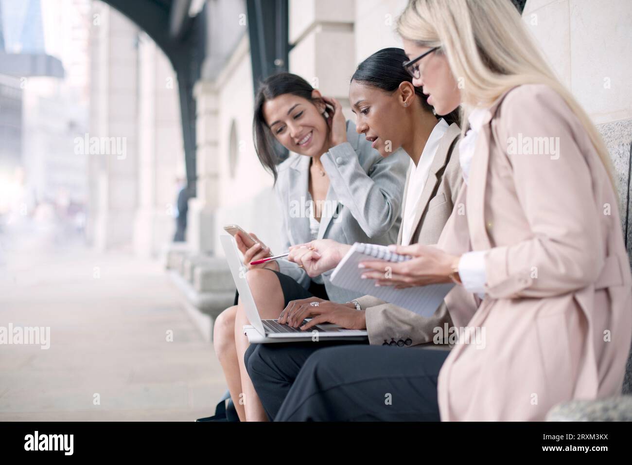 Colleagues using smart phone and laptop on bench Stock Photo