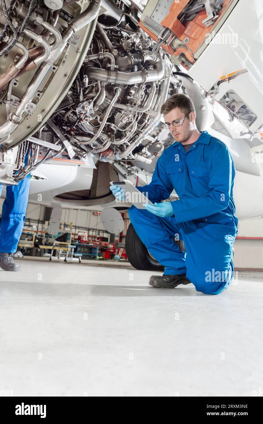 Crouched man using digital table by airplane Stock Photo