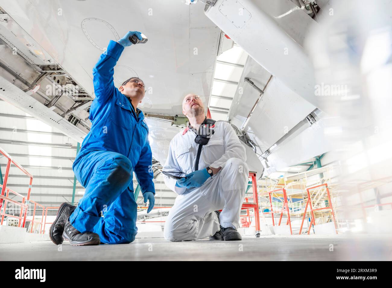 Kneeling men using torch underneath airplane Stock Photo Alamy
