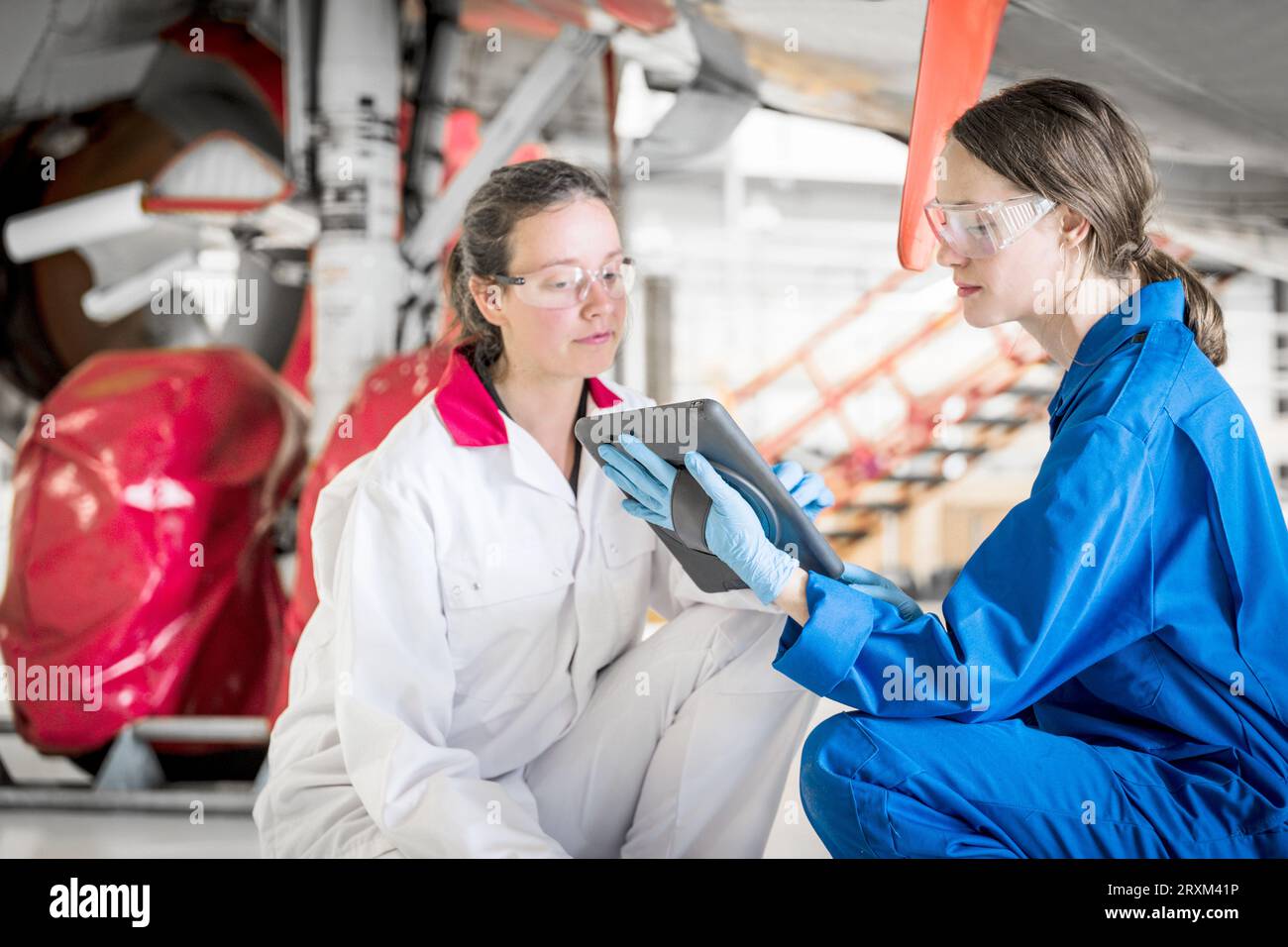 Crouched women using digital tablet under airplane Stock Photo
