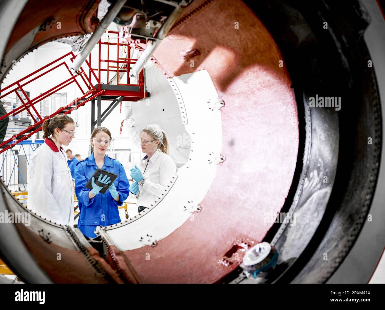 Female workers using digital tablet behind airplane engine Stock Photo