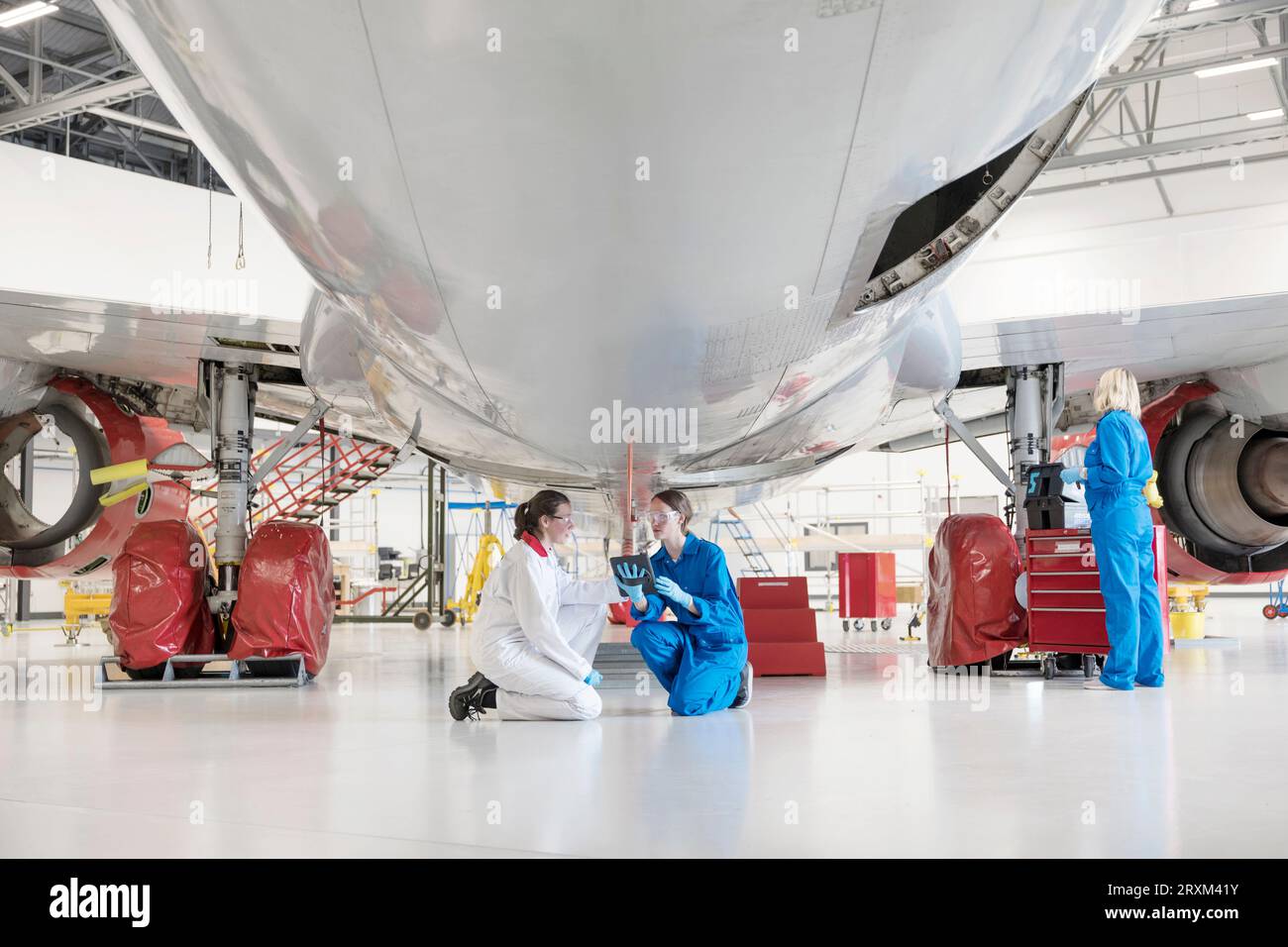 Crouched women using digital tablet under airplane Stock Photo