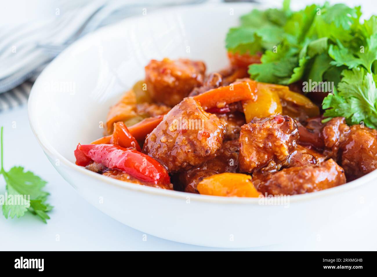 Stewed chicken fillet pieces with vegetables in a white bowl with cilantro. Stock Photo