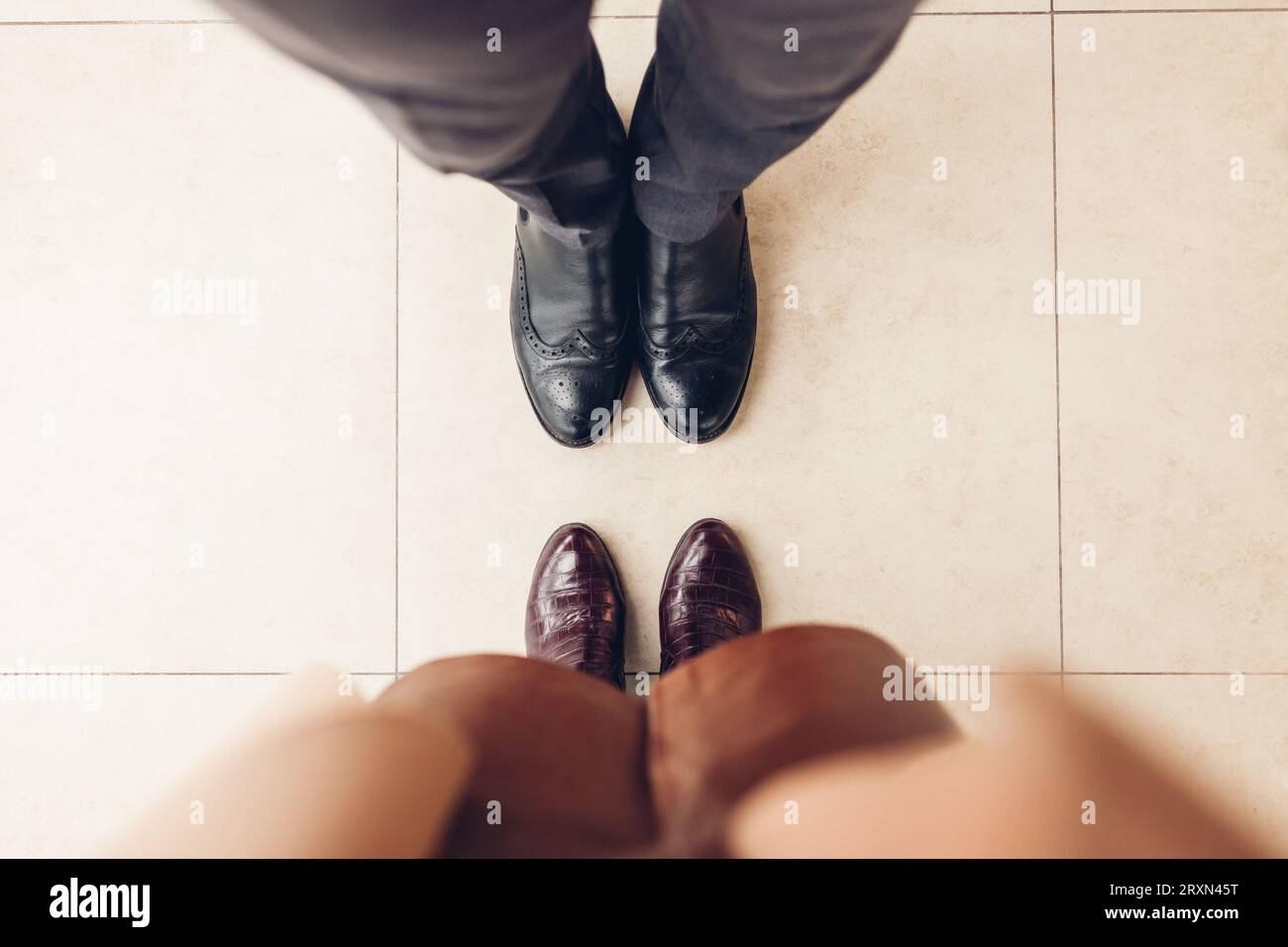Top view of couple's shoes. Man wearing black leather classic chelsea woman wears burgundy crocodile boots. Close up Stock Photo
