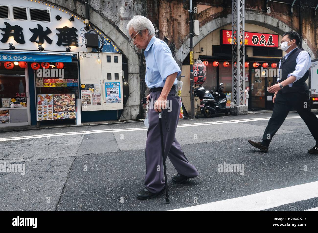 An elderly Japanese man walks along the road past some restaurants in Shimbashi, Tokyo, Japan Stock Photo