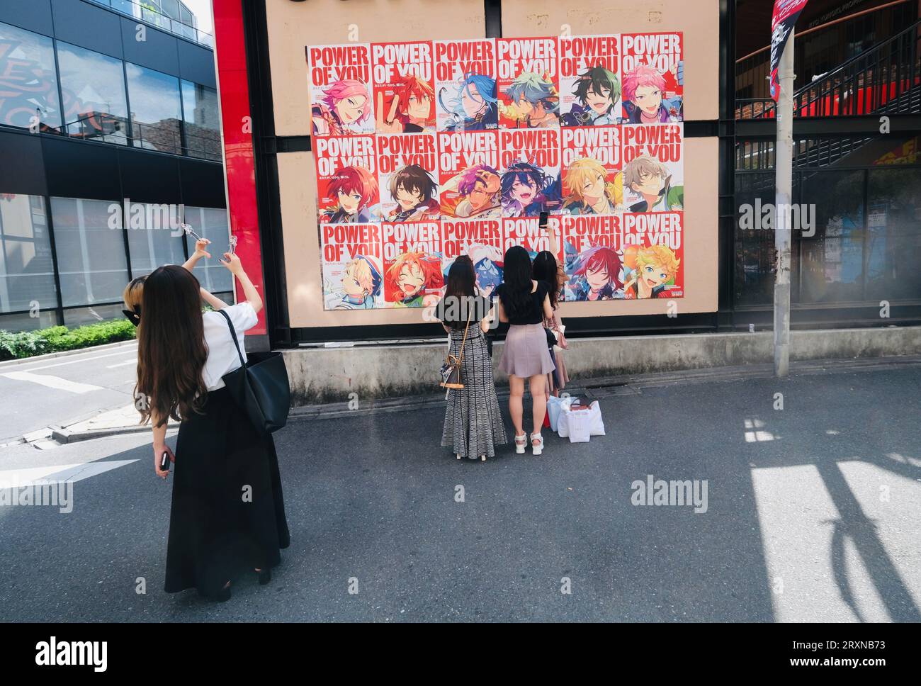 Japanese girls pose for photos beneath a Cosplay poster board in Shibuya, Tokyo, Japan Stock Photo