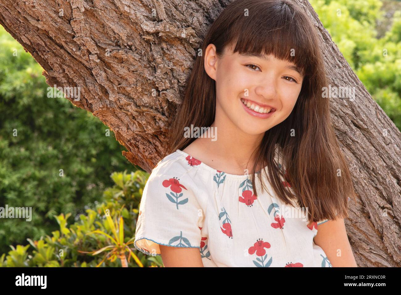 Eleven year old smiling girl leaning against a tree Stock Photo