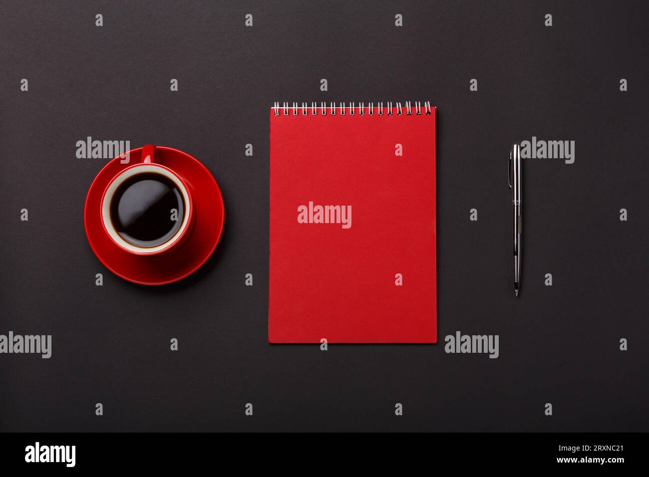 Black background red coffee cup notebook handle blank space desktop. Top view Stock Photo