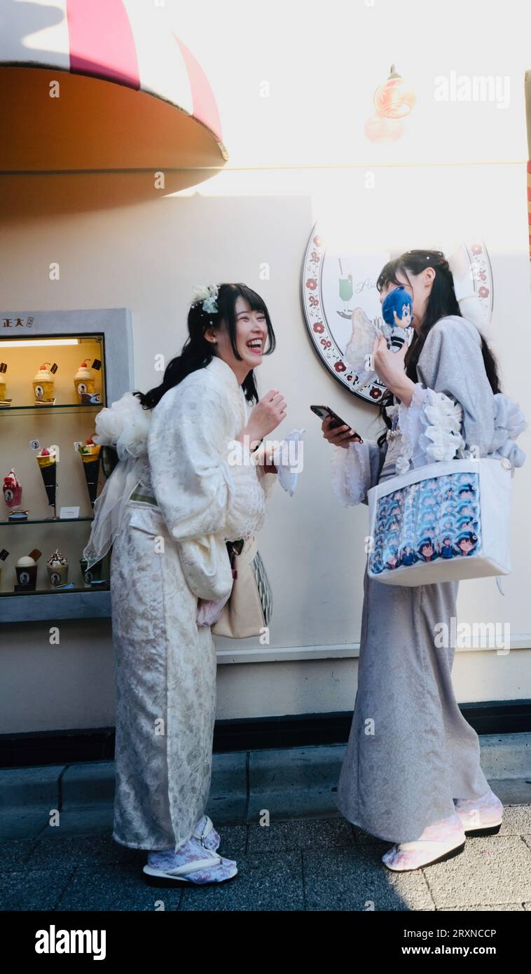 Two Japanese girls dressed in kimonos laugh at photos on a smartphone in Asakusa,Tokyo, Japan Stock Photo