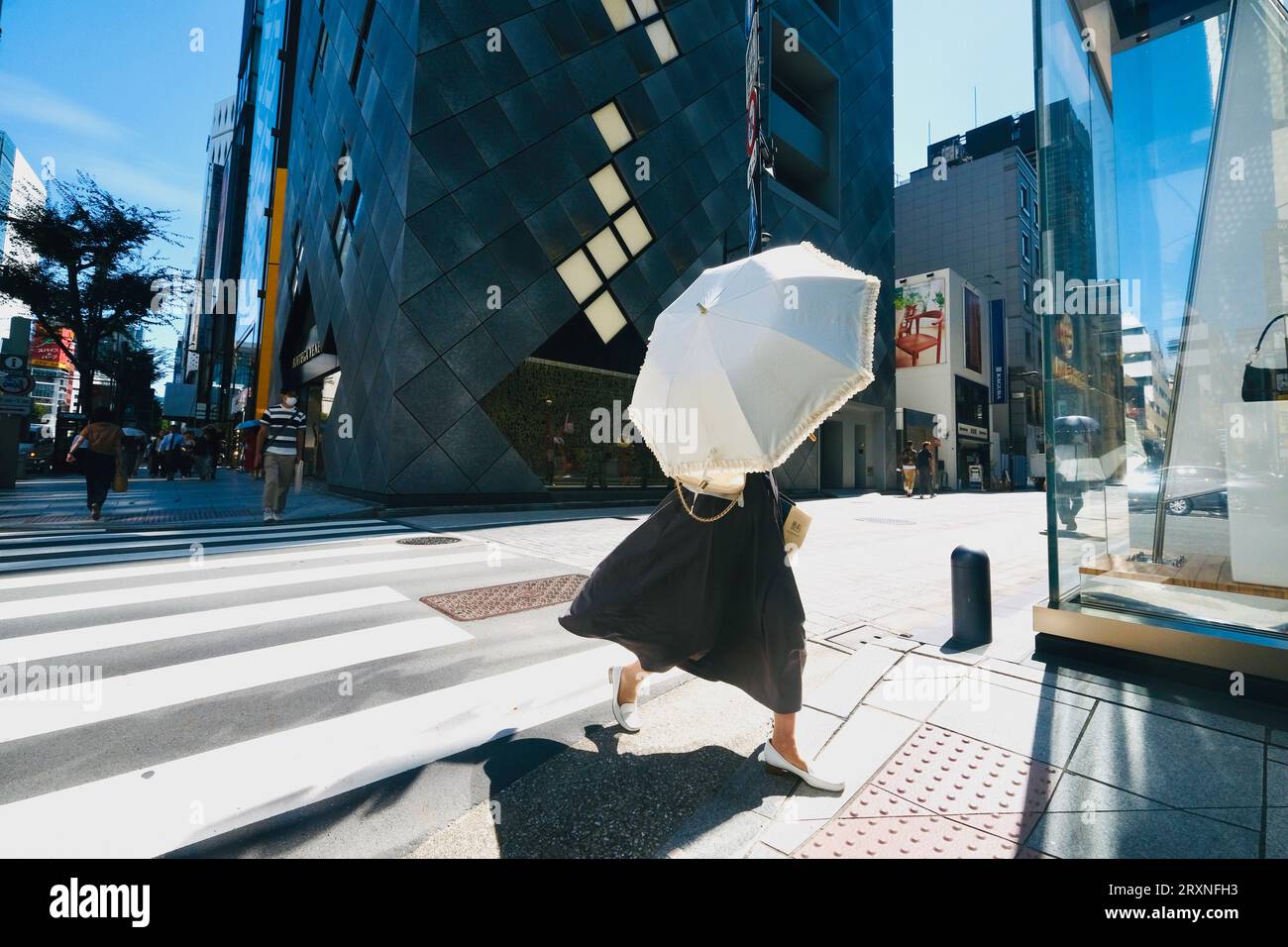 A woman holding an umbrella walks across a pedestrian crossing in Ginza ...