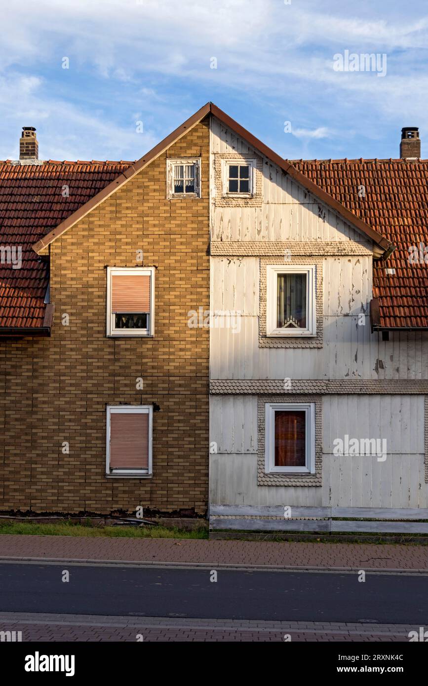 Old semi-detached house, run-down, dilapidated facade, dwelling house divided into two halves, cladding imitation clinker made of plastic and wooden Stock Photo