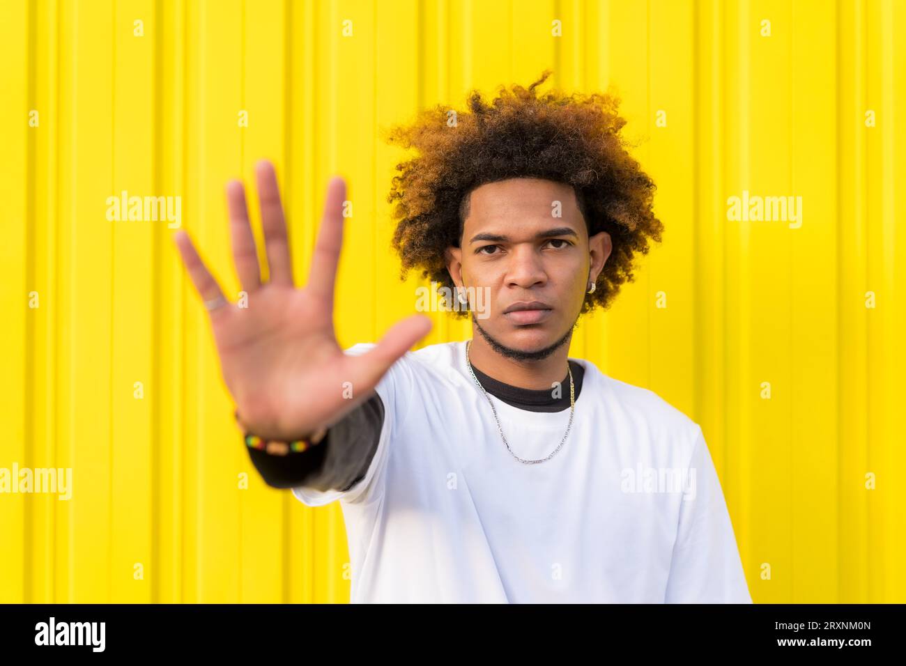 Horizontal photo with yellow background of a Mixed-raced young man gesturing stop with the hand Stock Photo