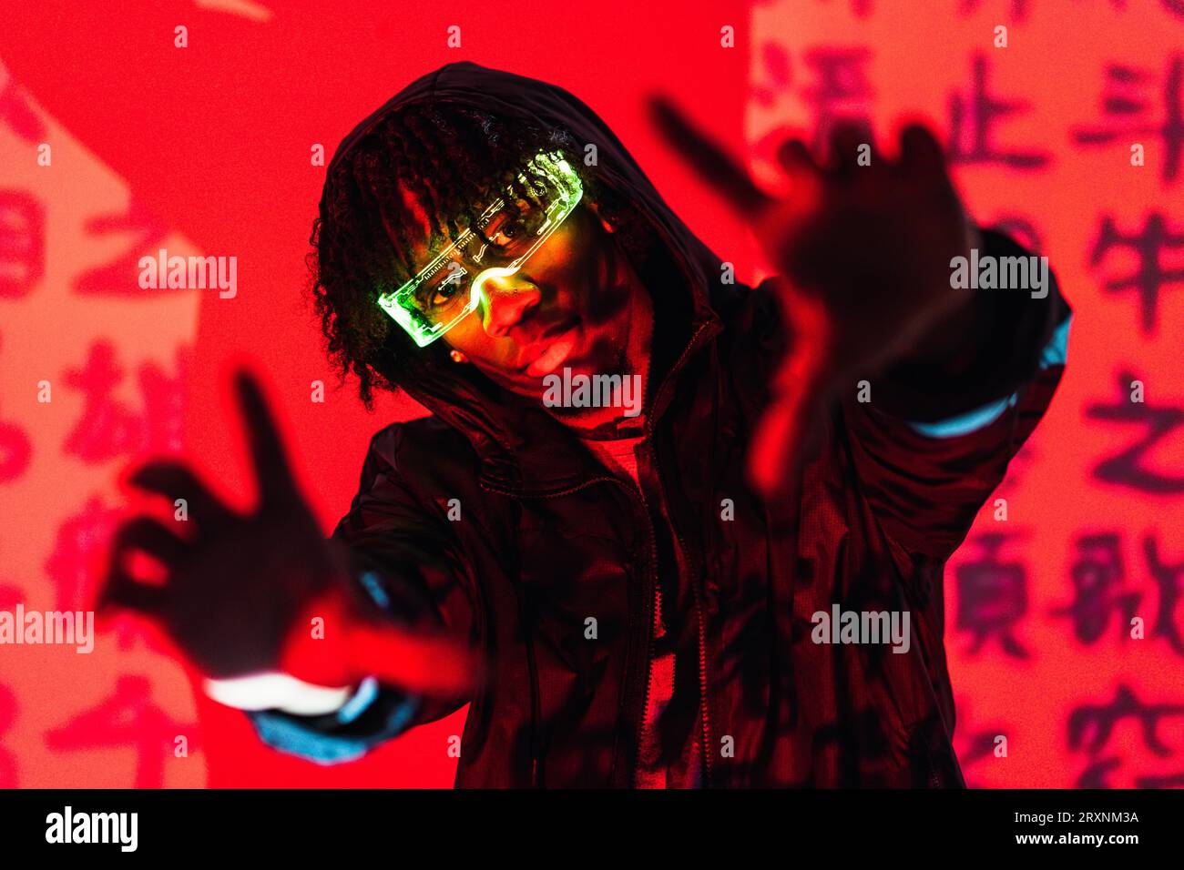 Studio portrait with red neon lights of a futuristic man wearing smart glasses gesturing and looking at camera Stock Photo