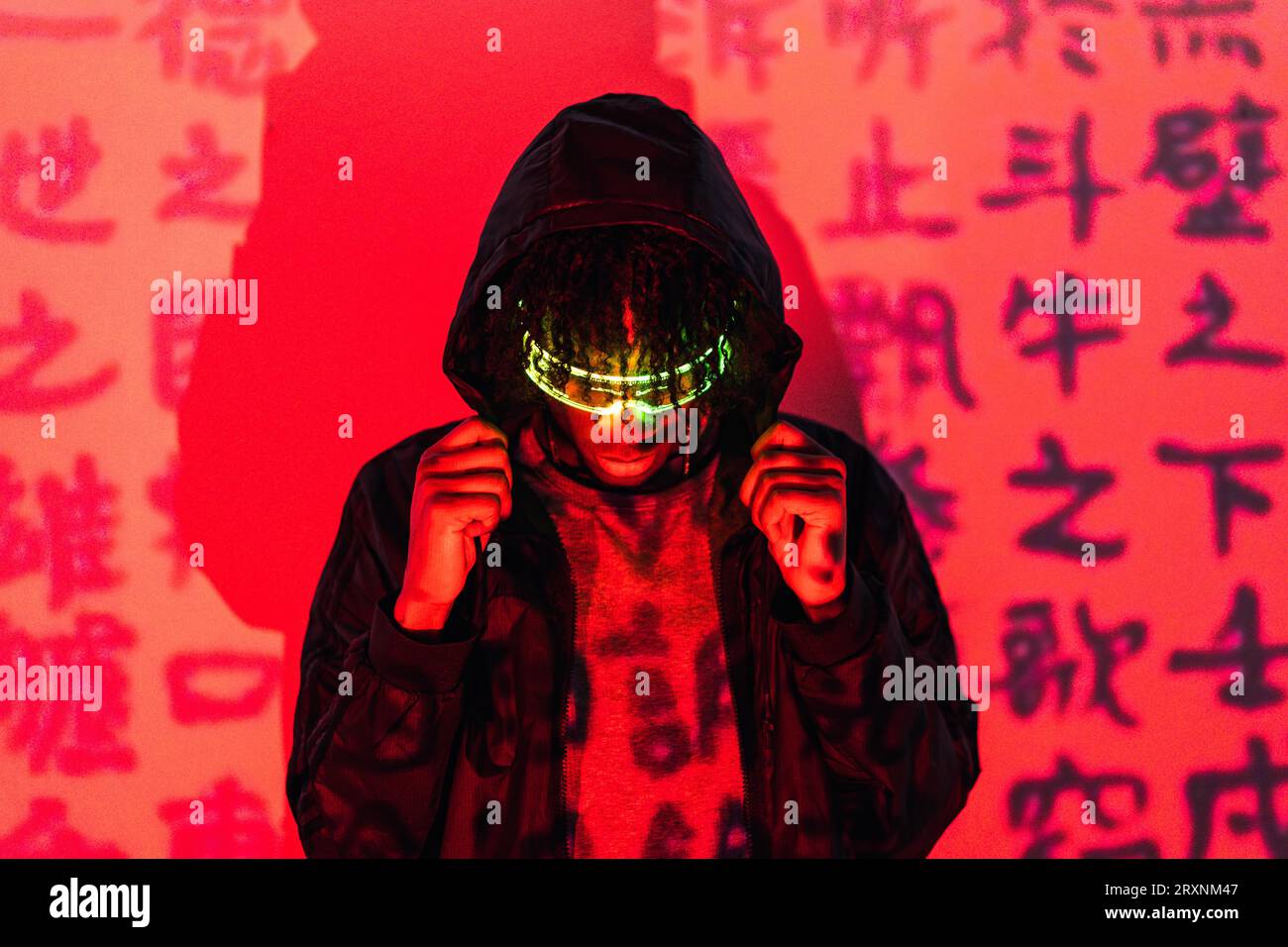 Studio portrait with red neon lights of an anonymous futuristic man wearing smart glasses hiding on a hoodie Stock Photo