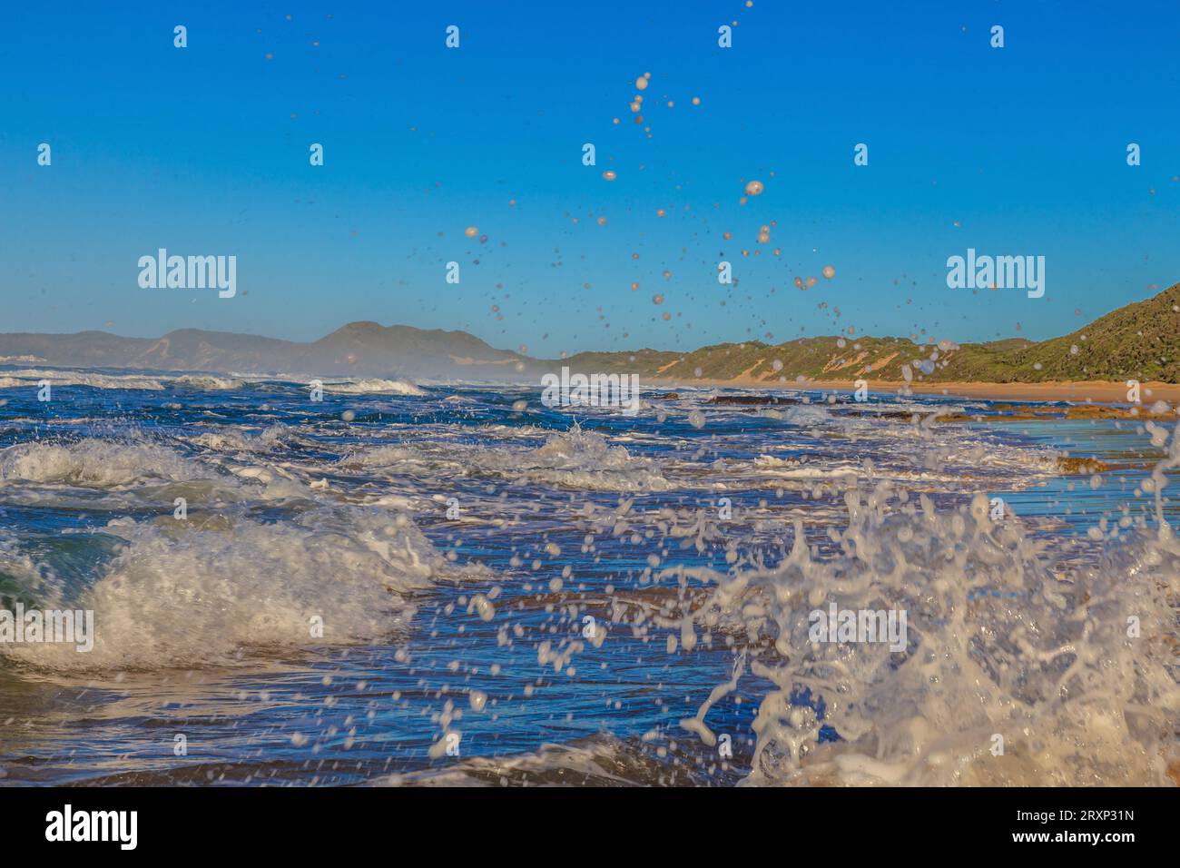 Footage of breaking waves with splashing water in the foreground photographed from a ground-near position in the morning at Brenton Beach in South Afr Stock Photo