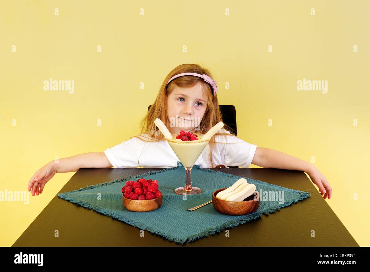 Cute little baby girl looking unhappy, she is not allowed to eat the dessert on the table in front of her. The concept of celebration. Stock Photo