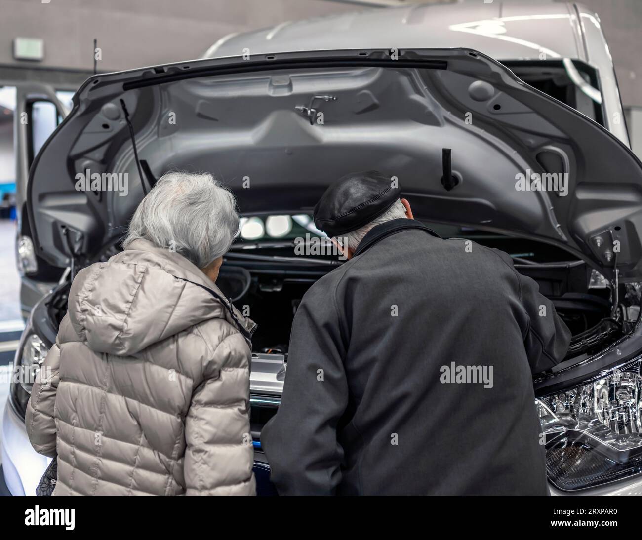 An elderly couple is interested in reliability of the technical design of a mini van looking at the engine and other components located under the open Stock Photo