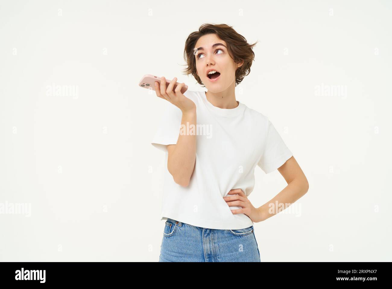 Portrait of chatty woman talking in speakerphone, records voice message on mobile phone and smiling, stands over white background Stock Photo