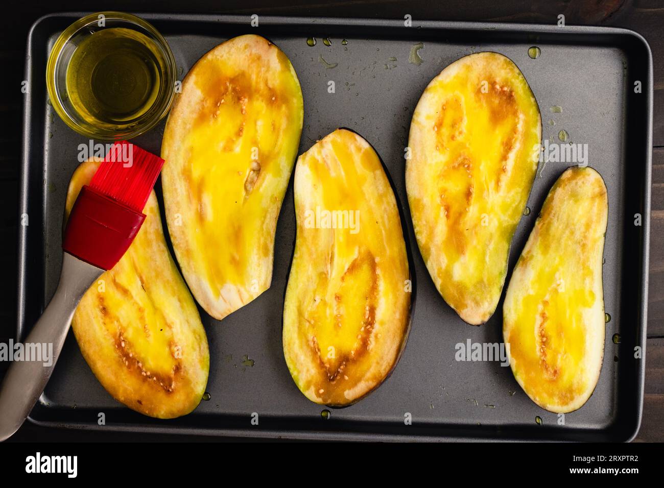 Eggplant Slices Brushed with Olive Oil on a Sheet Pan: Sliced of aubergine brushed with extra virgin olive oil on a baking pan Stock Photo