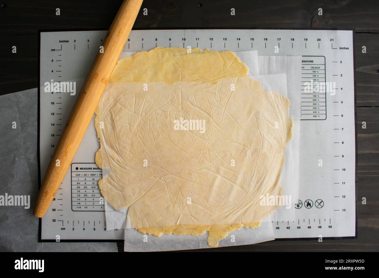 Rolling Out Pie Dough Between Sheets of Parchment Paper: Pie dough rolled out with a bamboo French rolling pin on a silicone mat Stock Photo