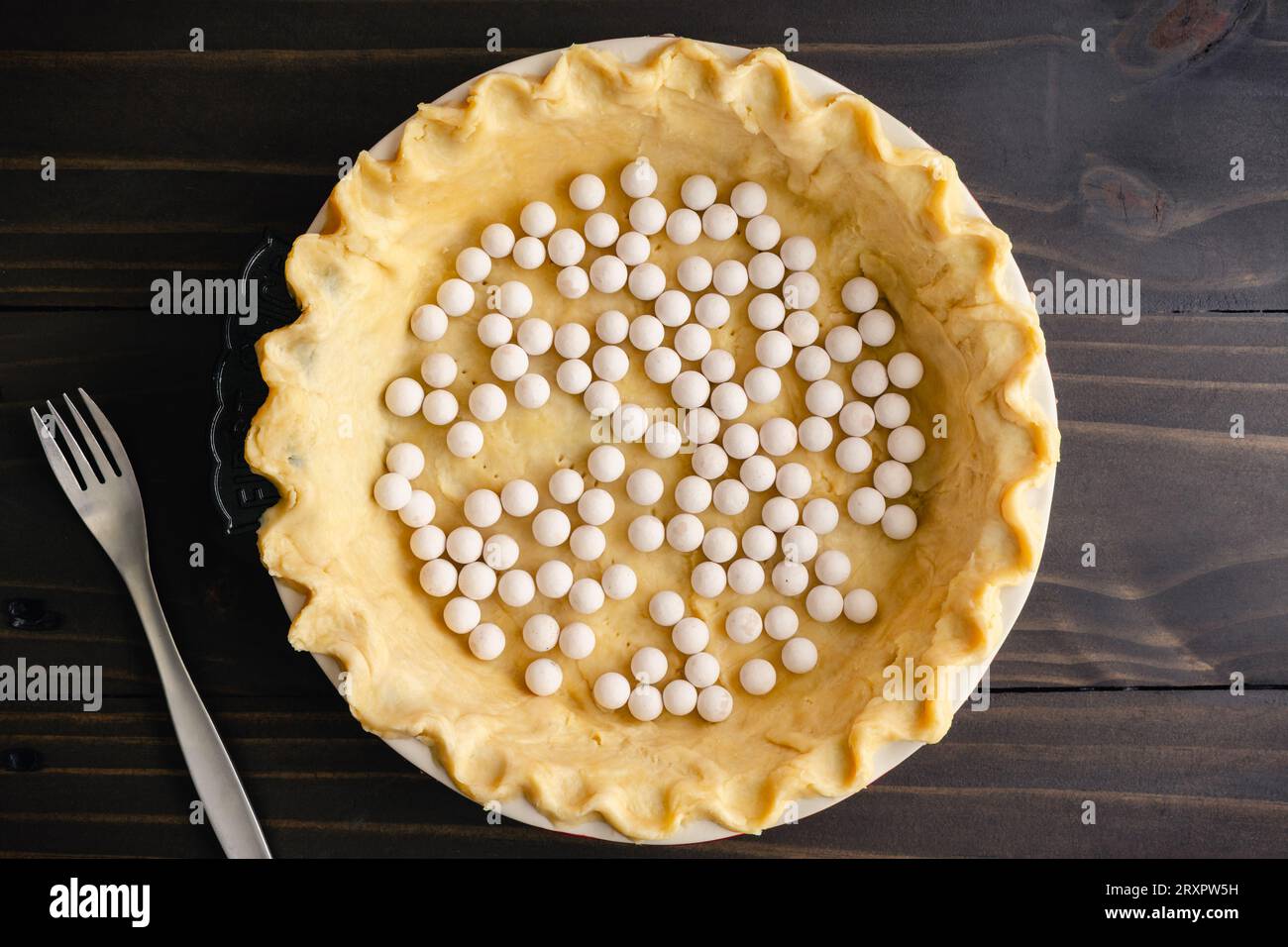 Unbaked Pie Crust Dough with Pinched Edges in a Pie Pan with Pie Weights: Raw dough with crimped edges in a deep ceramic dish with ceramic pie weights Stock Photo