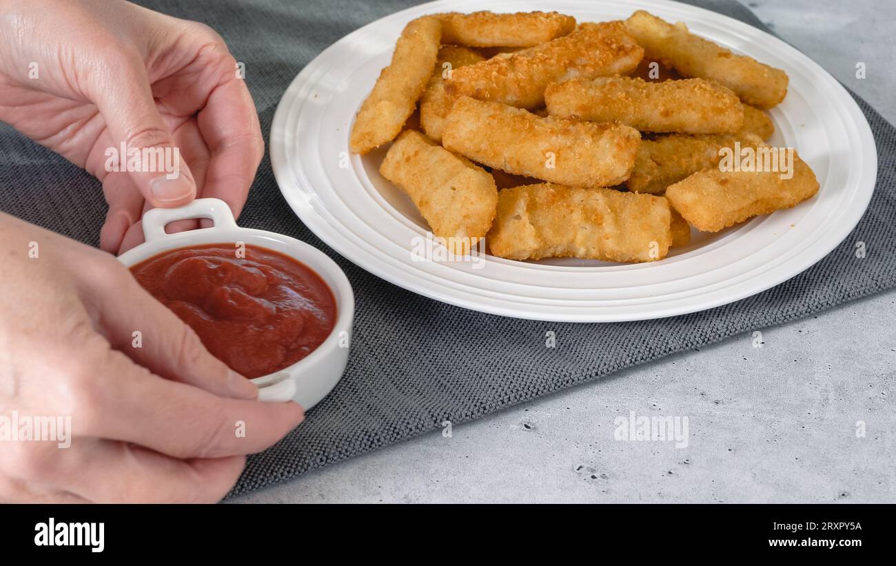 Fish sticks in a crunchy golden breading and bowl of ketchup closeup