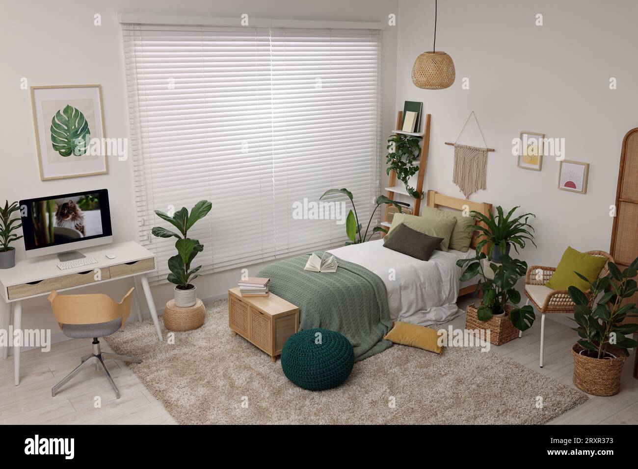 Comfortable bed, desk with computer and potted houseplants in stylish ...