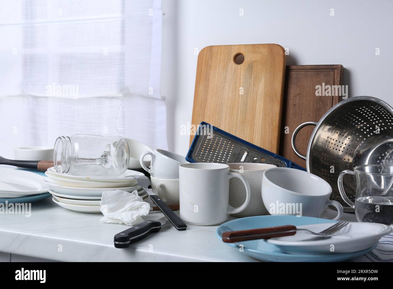 Many dirty utensils and dishware on countertop in messy kitchen Stock Photo