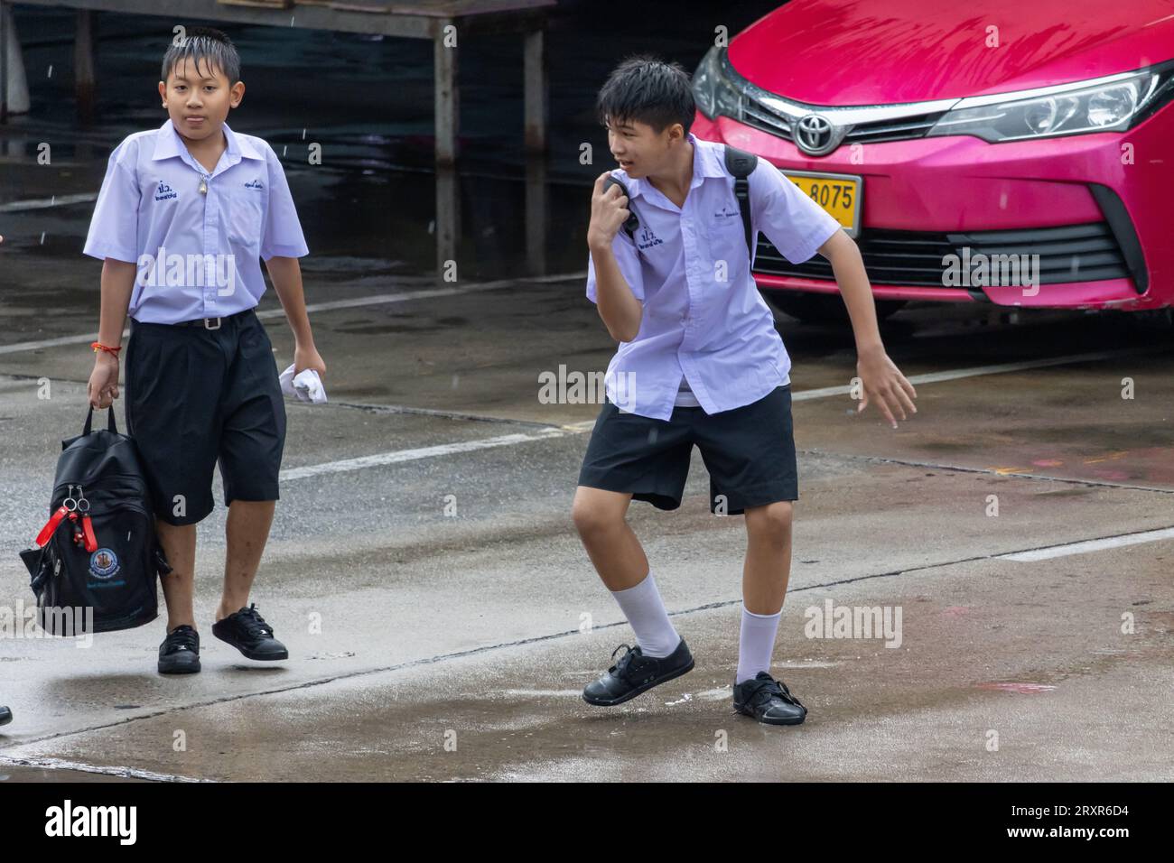 SAMUT PRAKAN, THAILAND, SEP 20 2023, Cheerful schoolboys in uniform play games on the rainy street Stock Photo