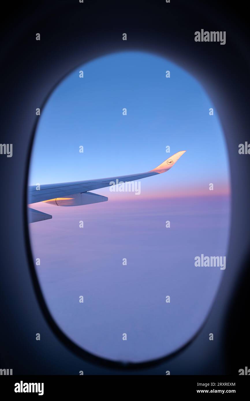 Lufthansa airplane wing seen through an oval window. View on a North Pole snowy landscape while flying the polar route. Vanilla sky. Stock Photo