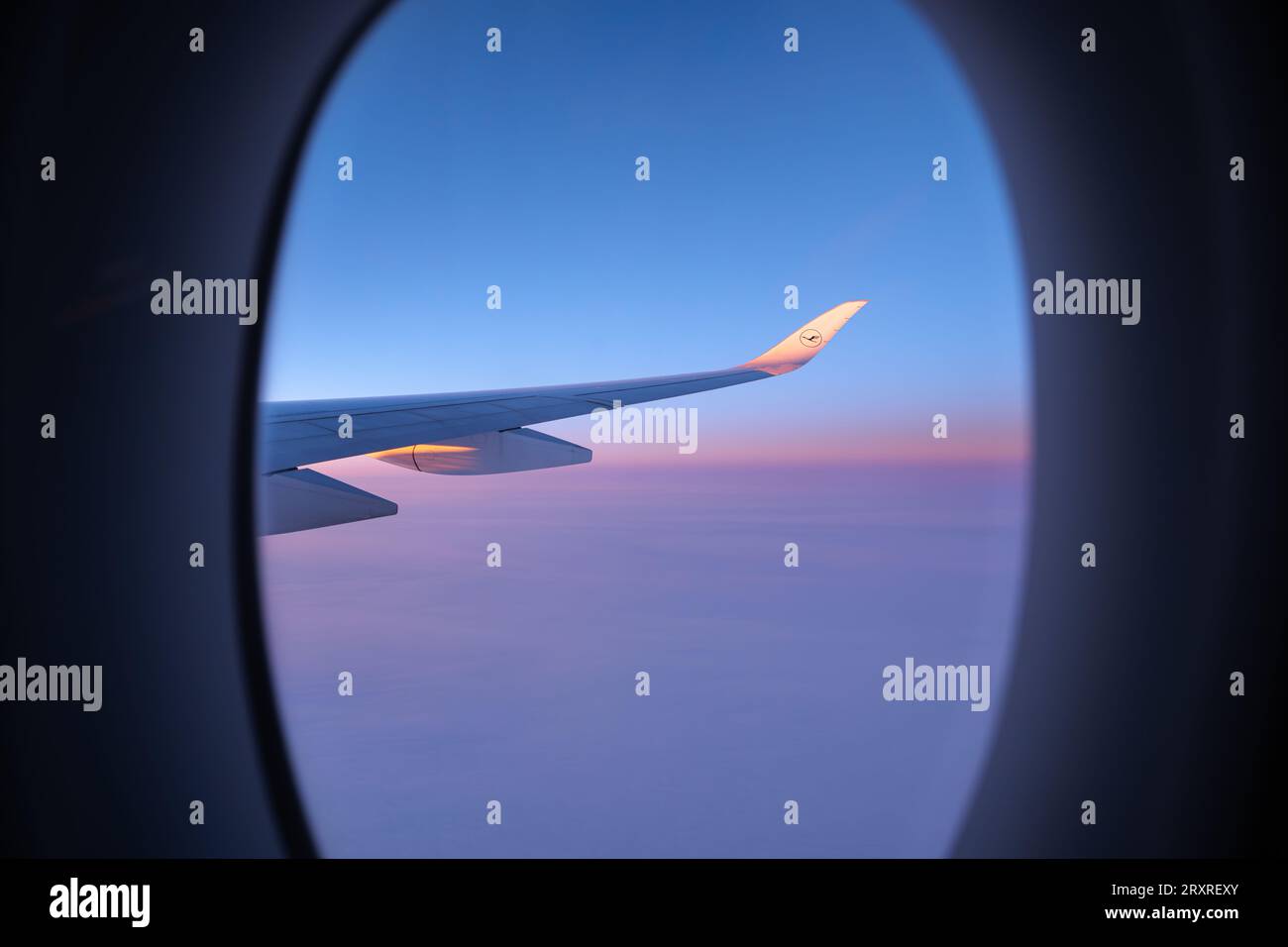 Lufthansa airplane wing seen through an oval window. View on a North Pole snowy landscape while flying the polar route. Vanilla sky. Stock Photo