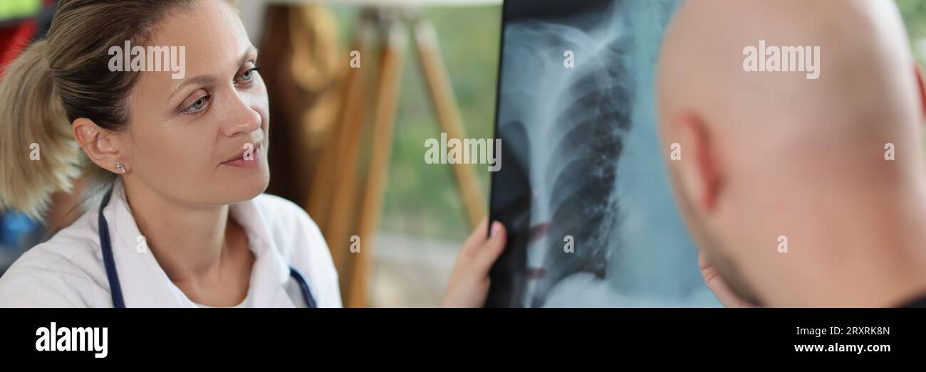 Female doctor holding x-ray image and pen in hands and speaking with male patient. Stock Photo