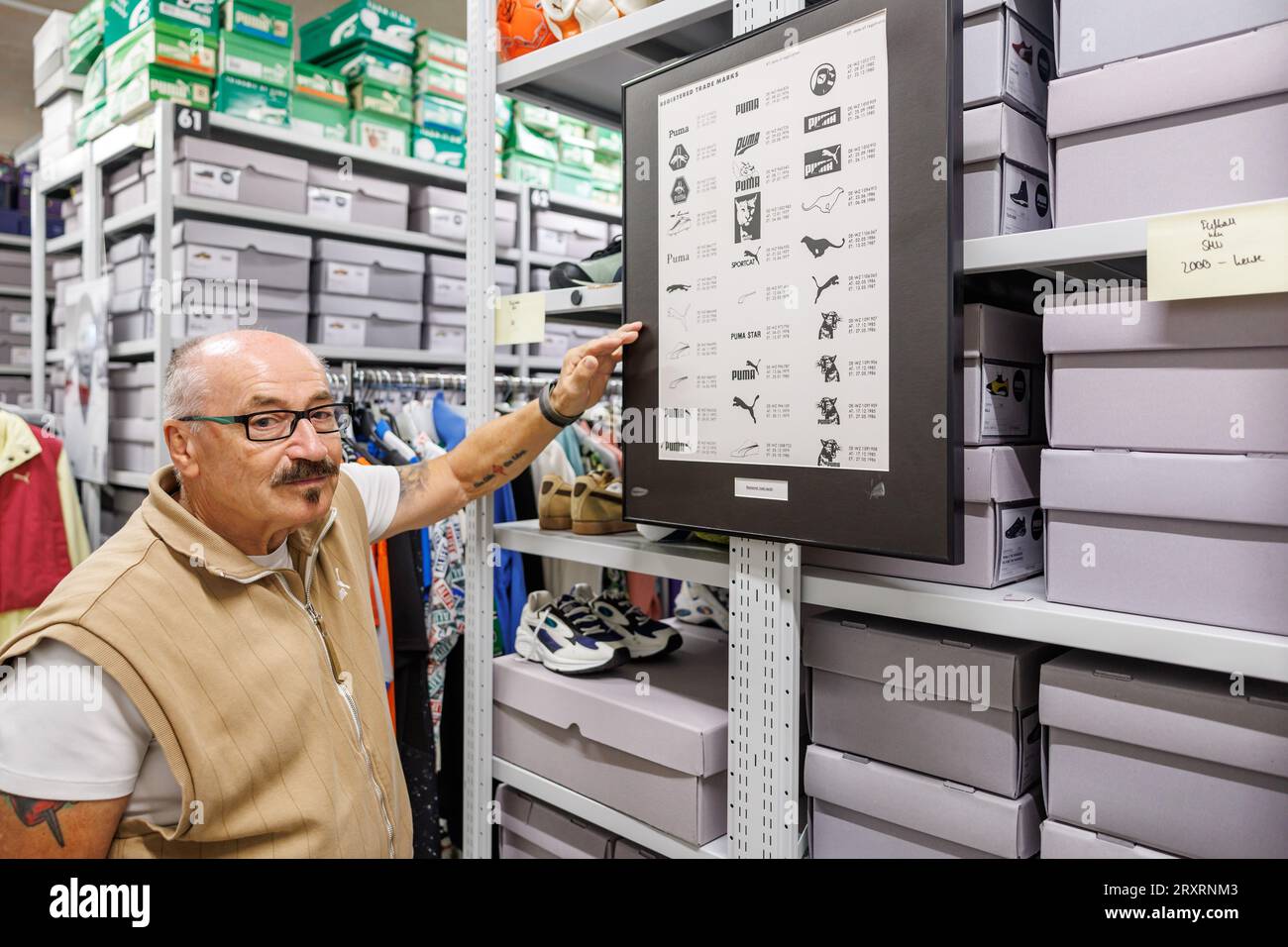 Herzogenaurach, Germany. 20th Sep, 2023. Helmut Fischer, a longtime  employee of sporting goods manufacturer Puma, stands in the archives at the  company's headquarters by a board with various designs of the Puma