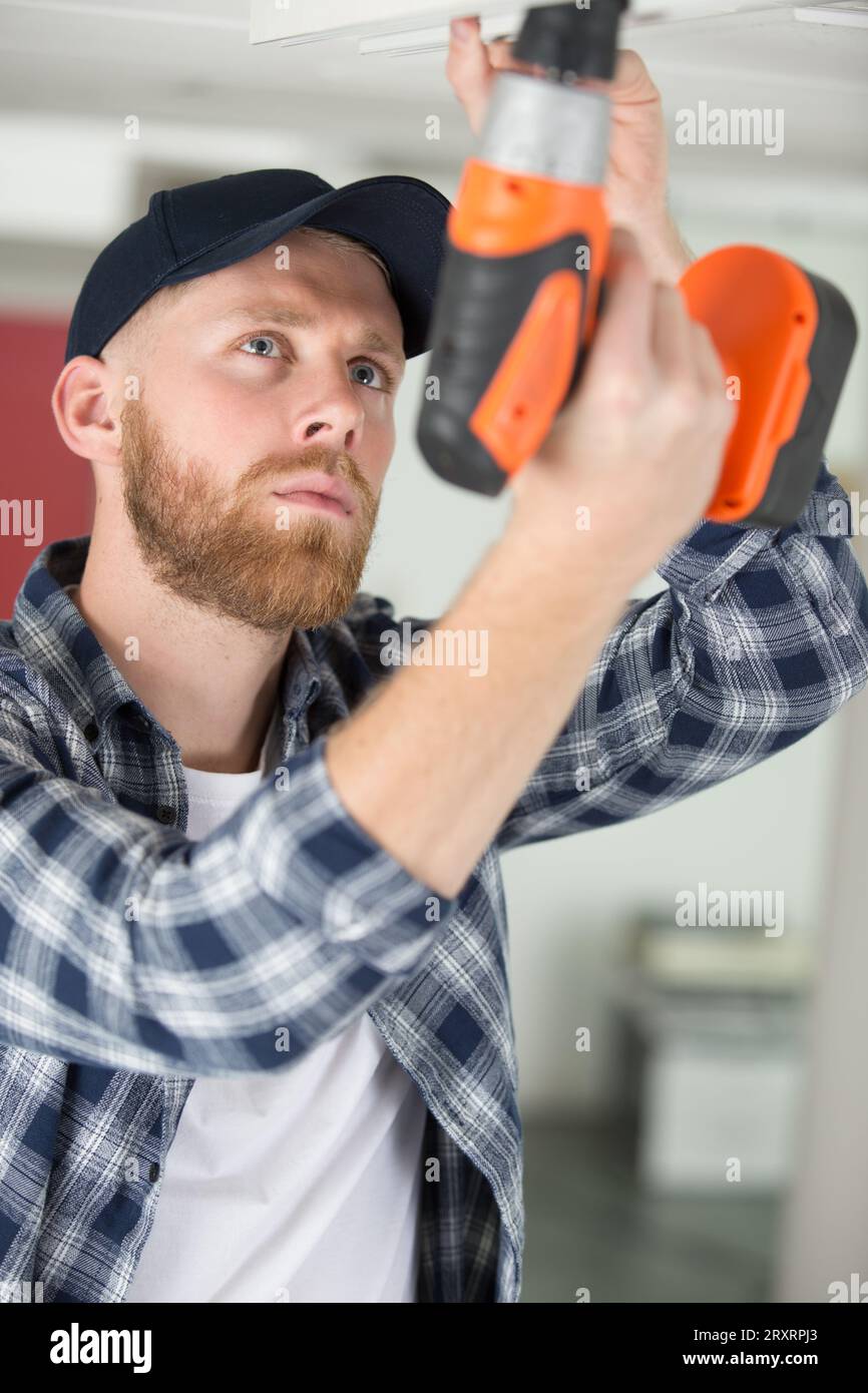 young concentrated worker drilling ceiling Stock Photo