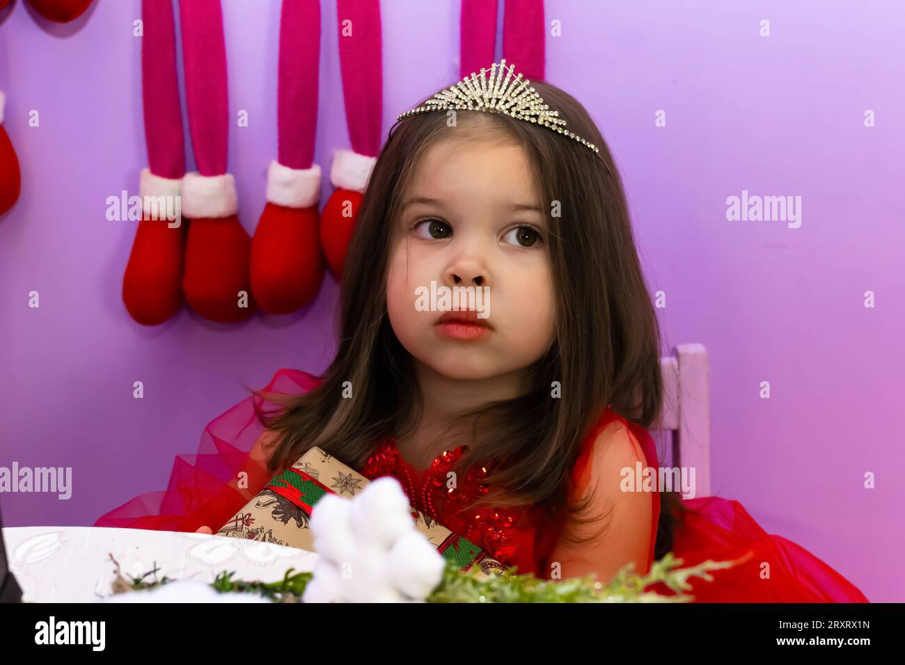 A little girl in a red dress is holding a gift. A little girl holds a ...