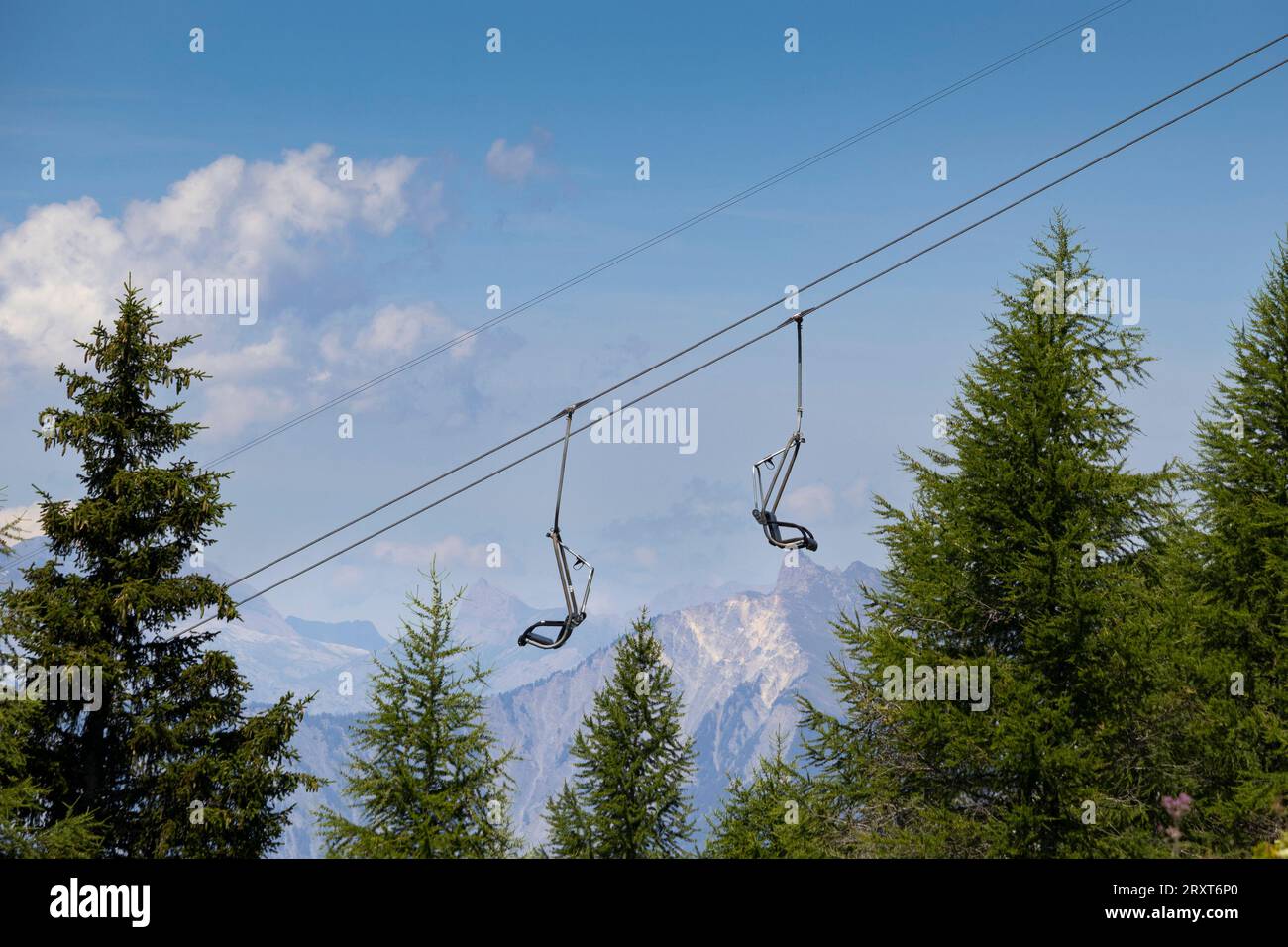 An empty ski chair lift in the summer, above the forest, with mountains in the background. Ski resort La Fouly in Switzerland. Copy space above. Stock Photo